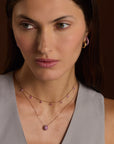 Woman wearing pink sapphire floating necklace and three sided hoop earrings against a brown background